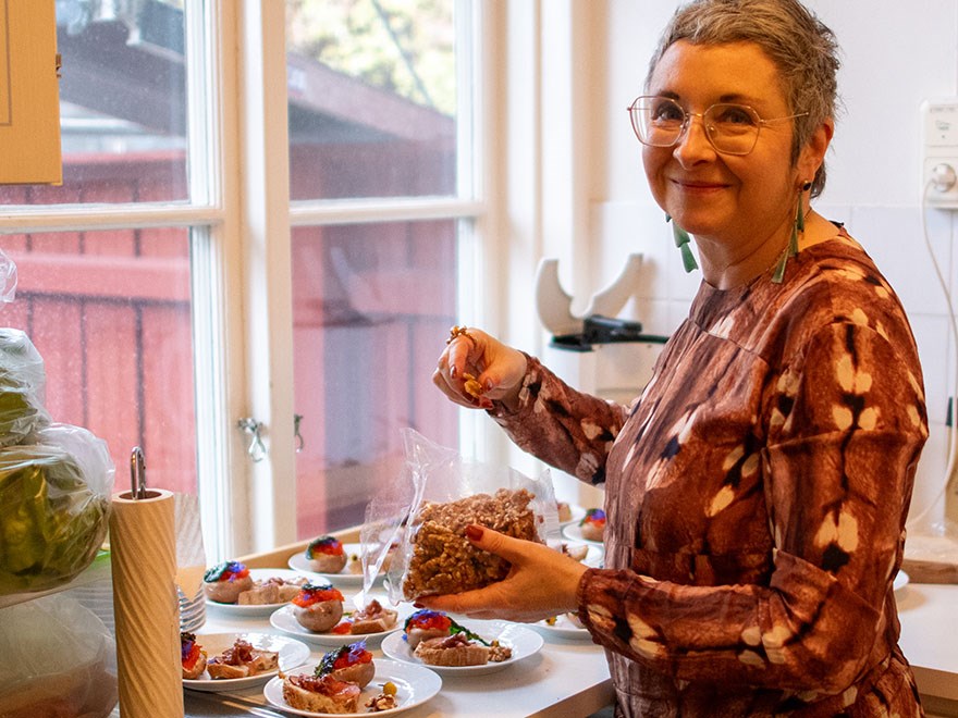 En kvinna ler mot kameran medan hon dekorerar assietter med mat. Foto.