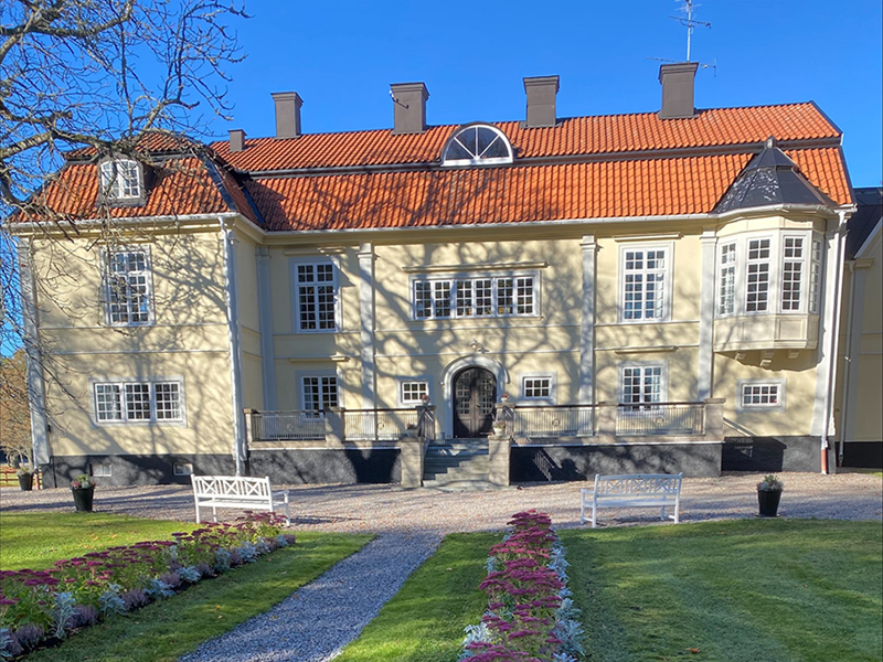 Ekenäs gård, en gulmålad byggnad i lantling miljö. Foto.