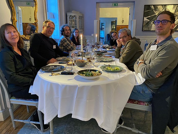 About 10 people are sitting around a table having dinner.