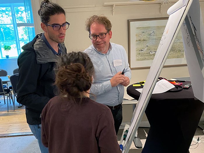 A woman and two men stand at a flipchart, drawing and writing.