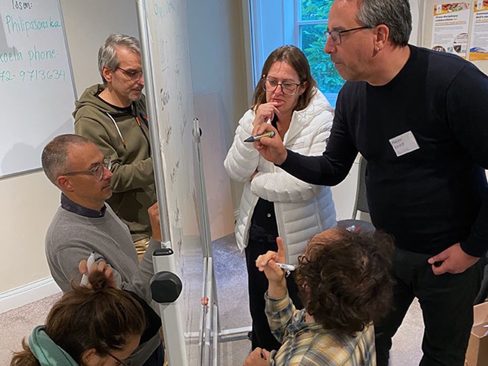 Six people stand at a flipchart, drawing and writing.