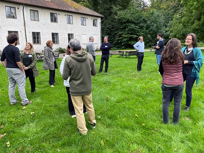 About 10 people are standing on a lawn talking to each other in pairs. 