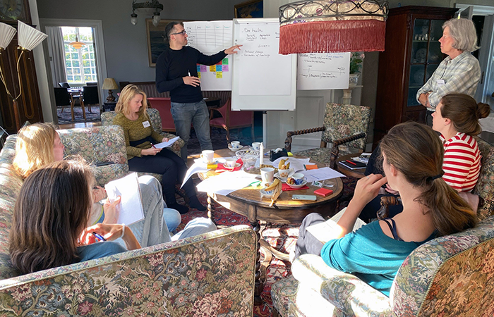 A group of researchers, men and women, report on a group project. They are in a room with old manor-style furniture, they have used post-it notes and flipcharts. Photo.