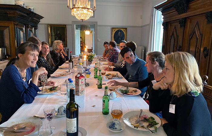 About 10 people, both men and women, sit at a large dinner table that is set for dinner. Photo.