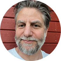 Close-up/headshot of a middle-aged man with grey hair and beard. Photo.