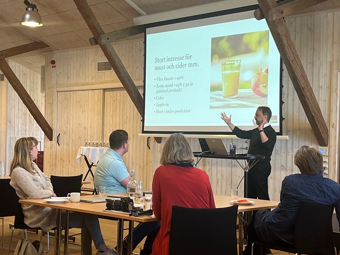 Jan Flemming Jensen från Kiviks Musteri AB  håller ett föredrag. På presentationen står det "Stort intresse för must och cider m.m."  I bakgrunden syns några workshopdeltagare.