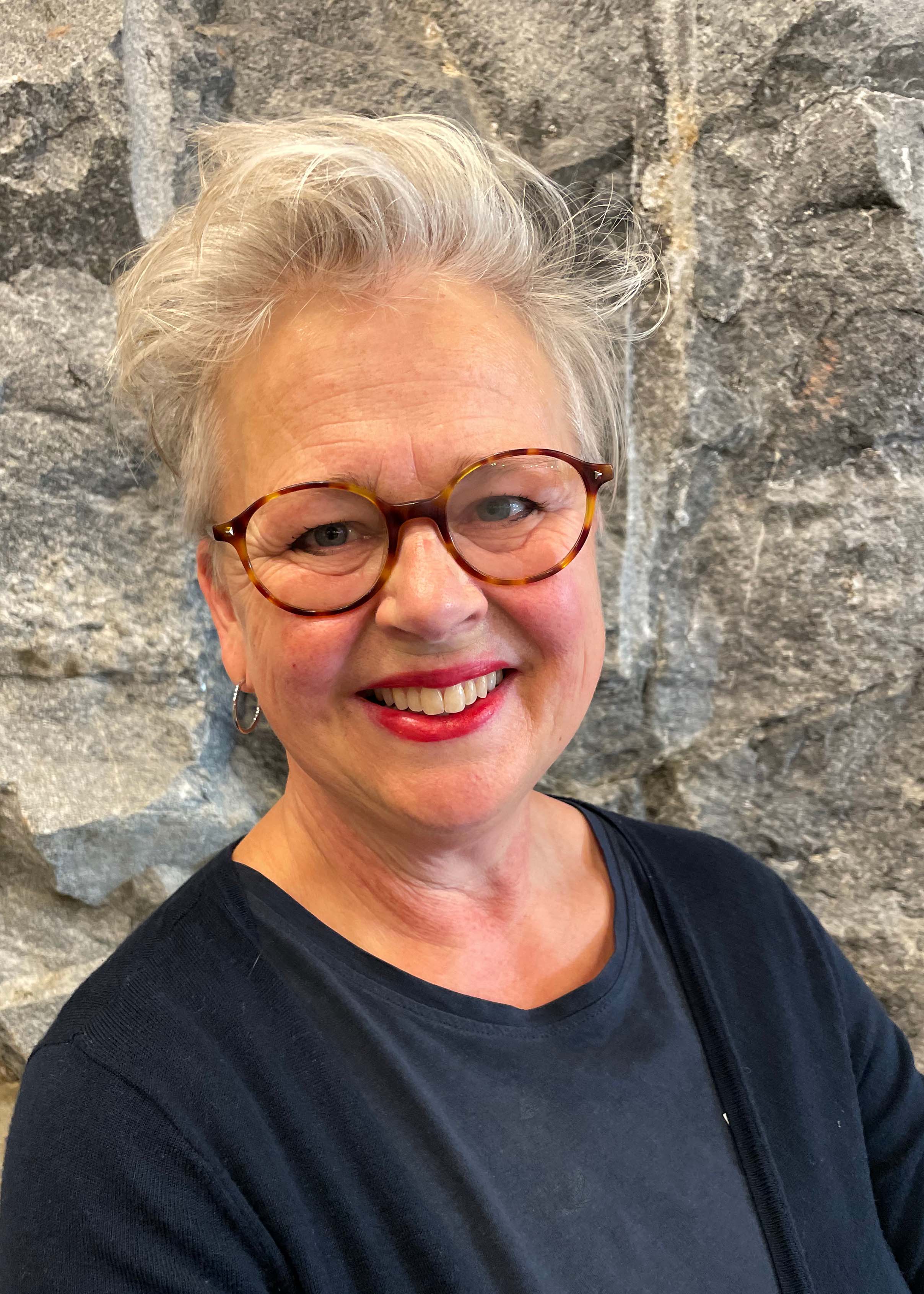 Portrait photo of smiling woman, glasses, silver grey hair, blue t-shirt