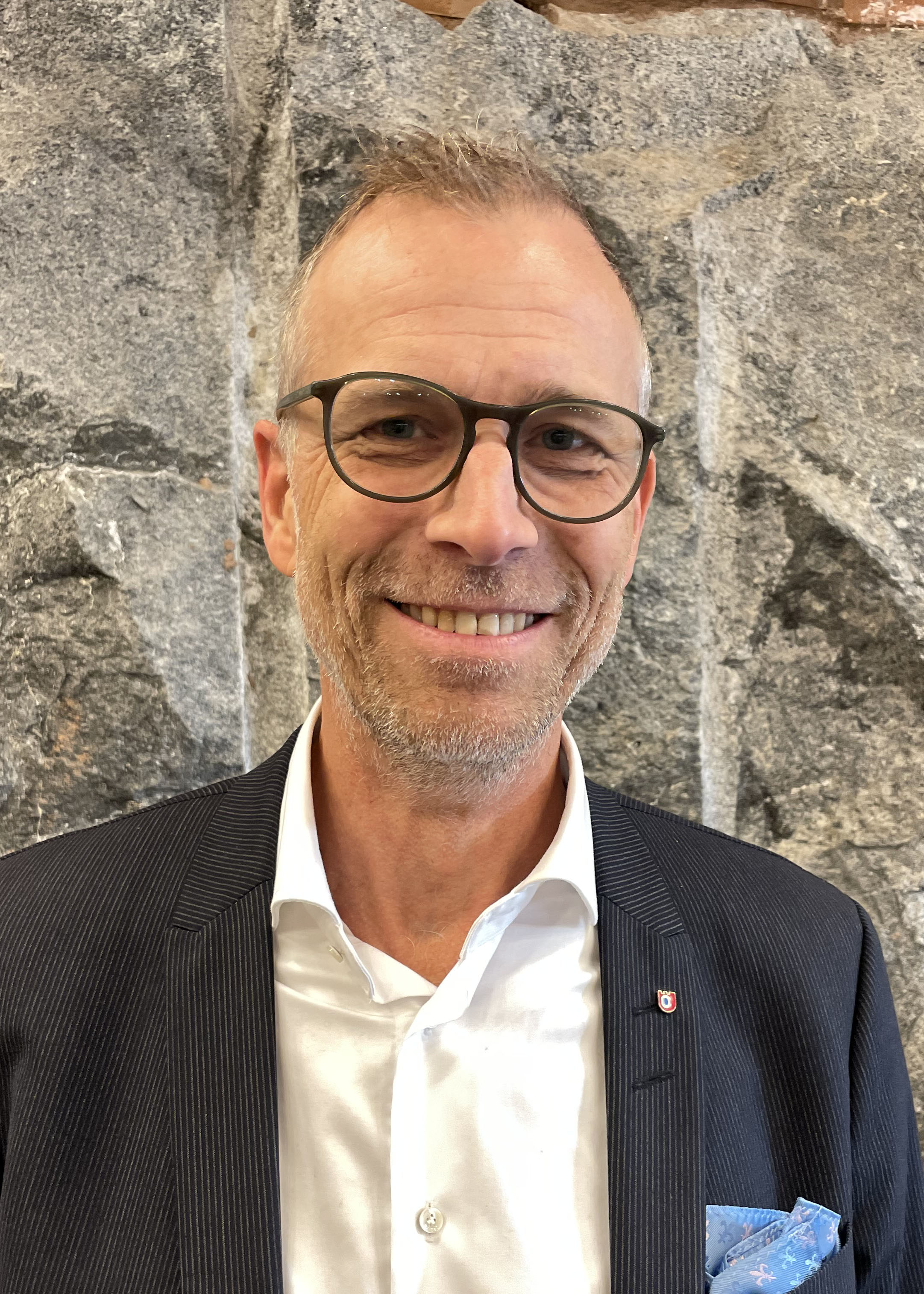 smiling man with glasses silver hair, dark suit and white shirt