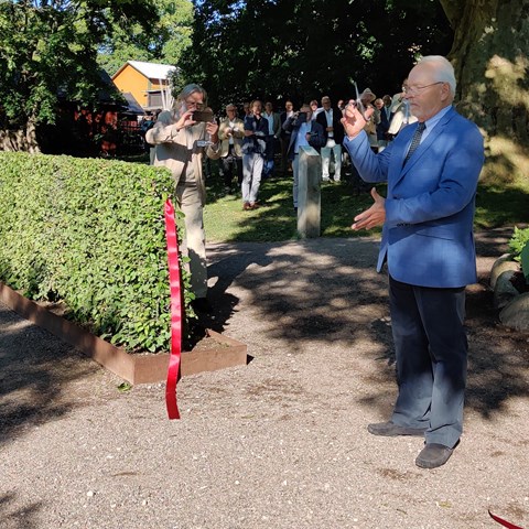 Invigning av klonarkivet vid DBW. Sven-Erik Lindström, ordförande i trädgårdsstyrelsen vid DBW, har just klippt av ett rött band in till klonarkivet och håller saxen i luften. I bakgrunden ses en skara finklädda människor som applåderar.  