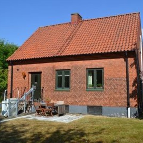 Färgfoto av Trädgårdsmästarbostaden där Nationella genbanken har sina kontor. På fotot syns ett rött tegelhus med tak av rött tegel. På framsidan av huset syns en grön trädörr och två fönster med grönmålade bågar.
