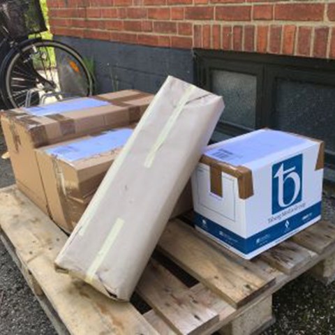 Paket av olika storlekar står på en lastpall framför genbankshuset. 