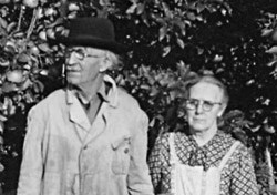 Svartvitt foto som visar ett äldre par som står framför en hög häck. 