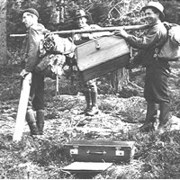 Three men in the woods carrying a coffin. Photo.