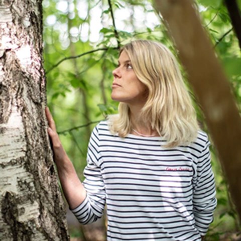A woman stands by a birch in the forest. Photo.