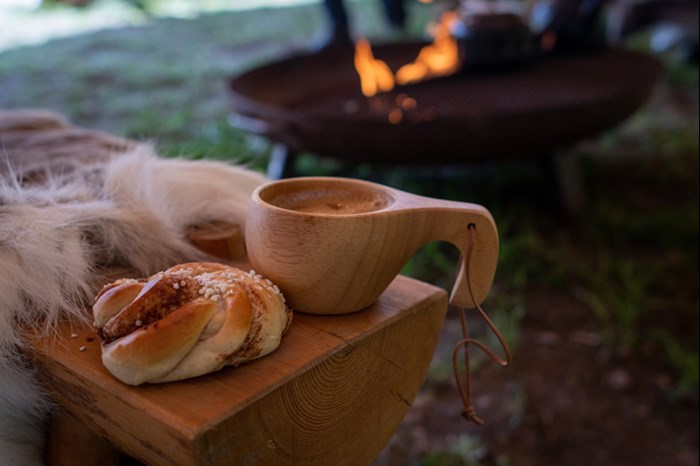 En kåsa och en kanelbulle på en bänk. Foto.