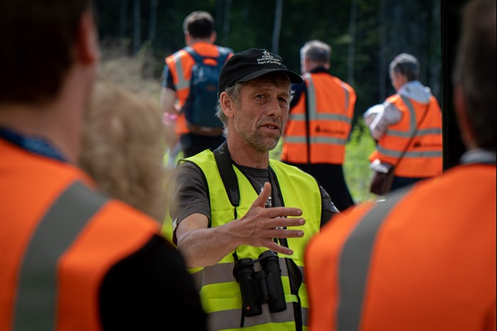 En person med keps berättar framför andra personer. Foto.