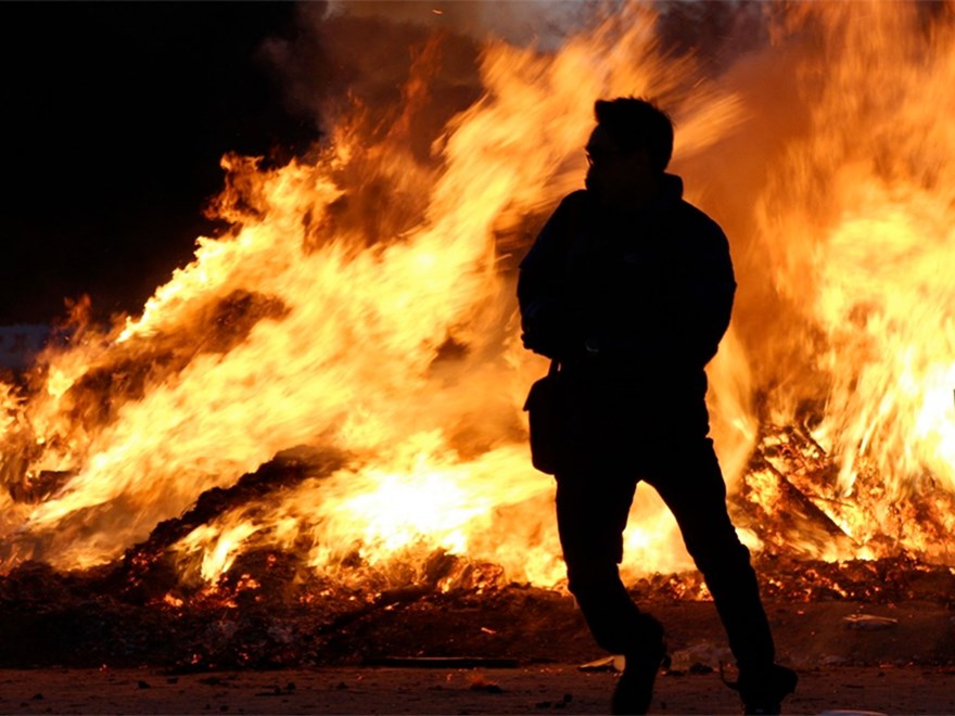 A man in front of a large fire. Photo.