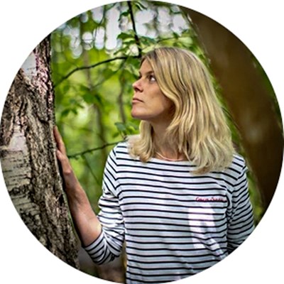 A woman by a tree in a forest. Photo.