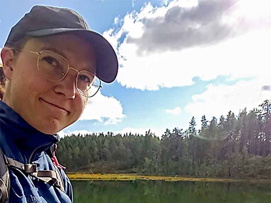 Porträttfoto av en kvinna. I bakgrunden finns skog och vatten. Foto.