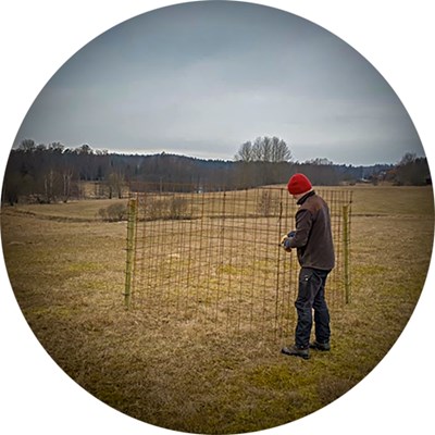 A man by a cage outdoors. Photo.