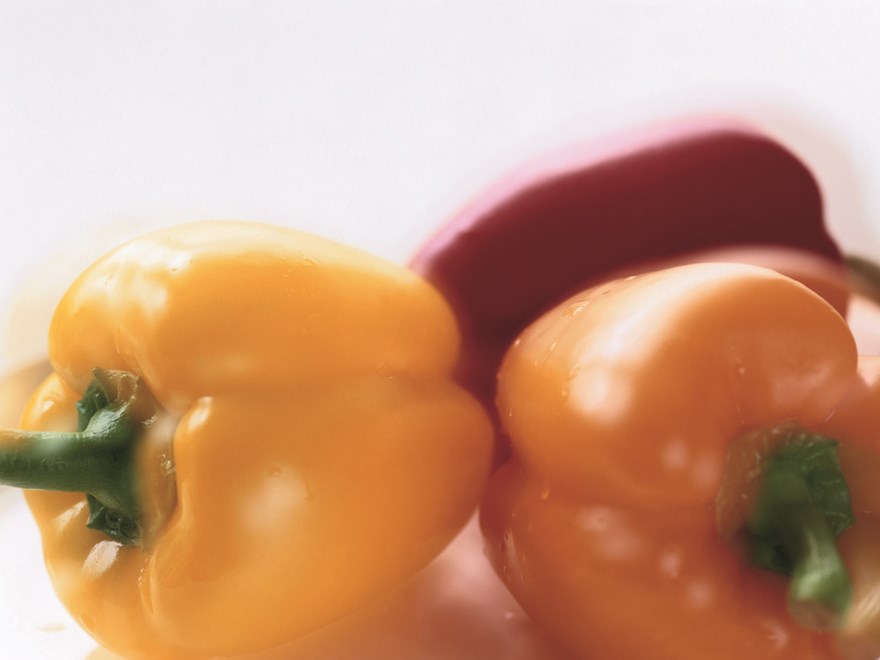 Närbild på tre olikfärgade paprikor, en gul, en orange och en röd, foto.