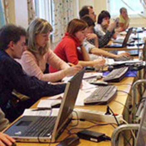 Personer som arbetar vid sina datorer i en föreläsningssal. Foto.