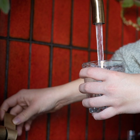 Två  händer fyller på vatten i ett glas, från en kran.