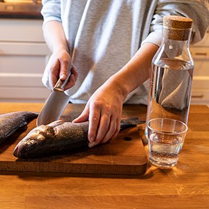 A person cleans fish. On the table is a bottle and a glass of water.