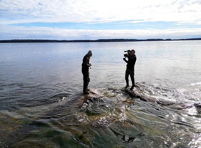 Två personer stående på klippa med havet i bakgrunden