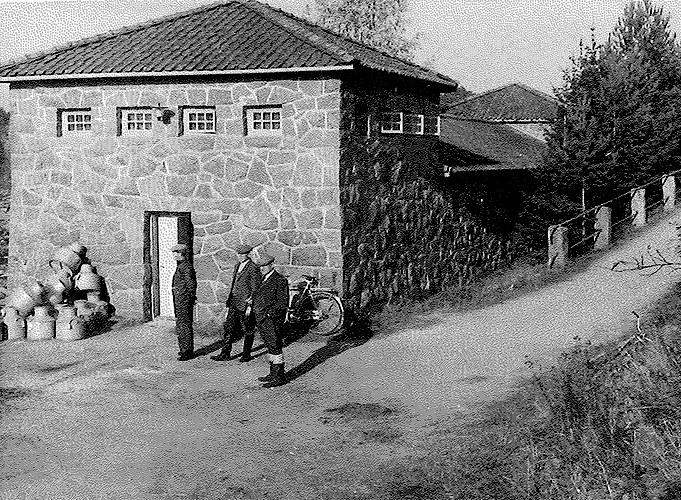 Tre män står framför en stenbyggnad. Foto.