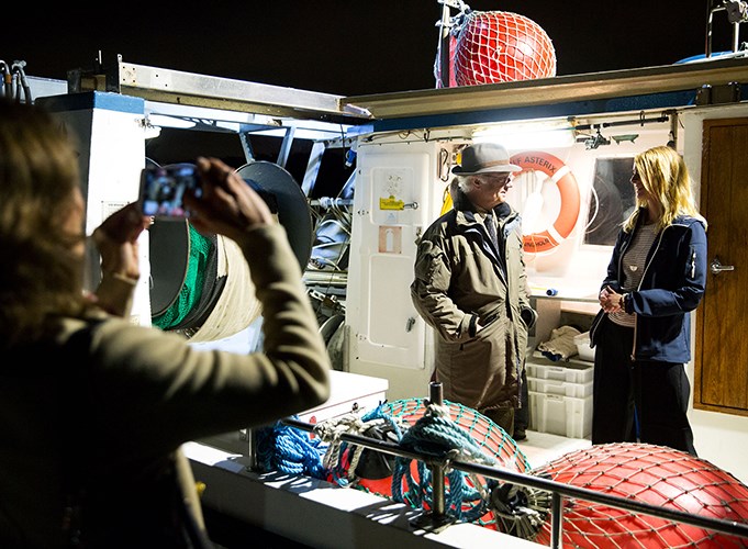 Carl XVI Gustaf samtalar med avdelningschefen på sötvattenslaboratoriet ombord på båt. En person fotograferar. Foto, beskuren.