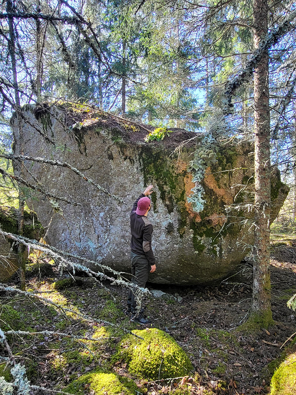 En person som står brevdid en stor sten i skogen. Foto.