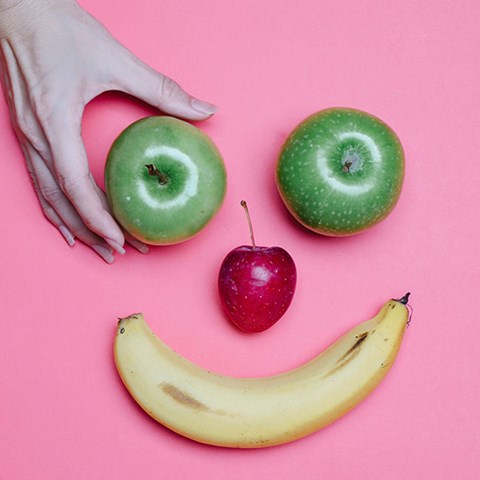 Ett ansikte gjort av frukt. Äpplen är ögon och en banan är munnen.