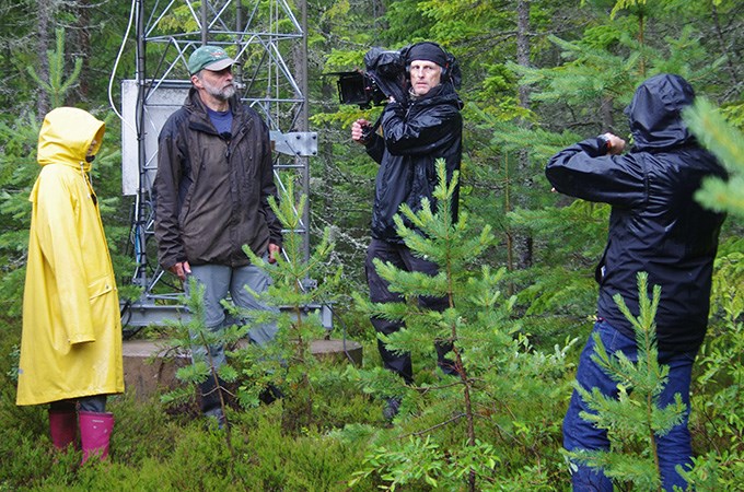 Man with big camera films some people in the forest.
