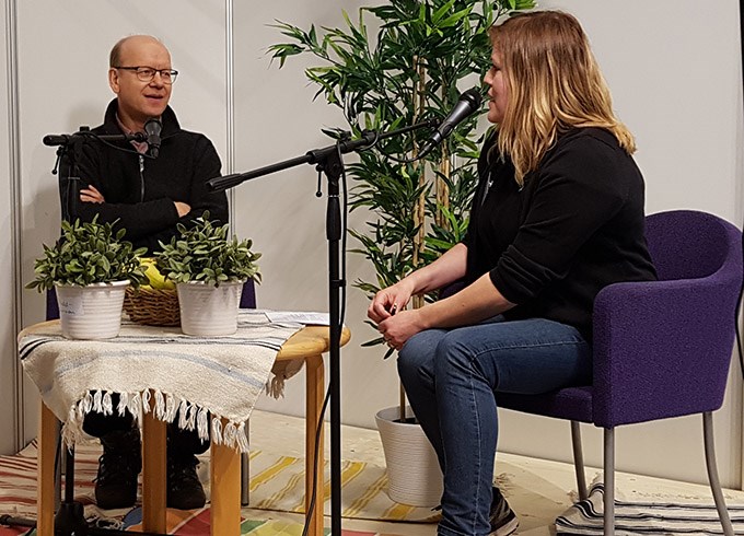 Kvinna intervjuar man på podium.