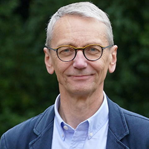 Man med grått kort hår och glasögon klädd i blå kavaj