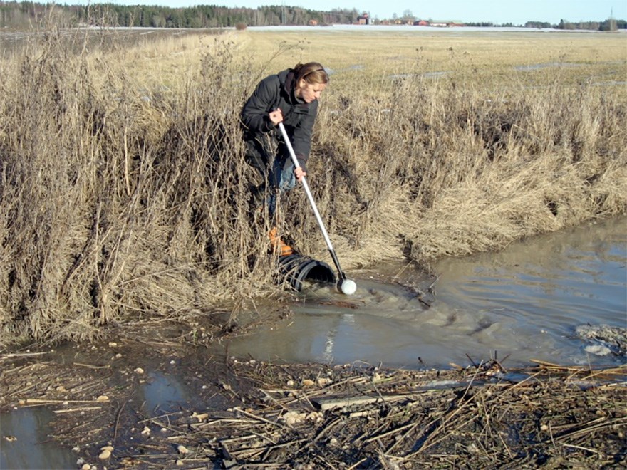 A person at the edge of a river takes water samples, photo.