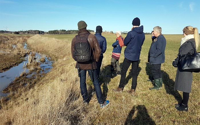 Flera personer står vid ett jordbruksdike, foto.