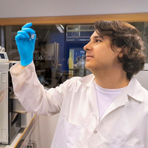 En man håller upp ett provrör i labbmiljö. Foto.