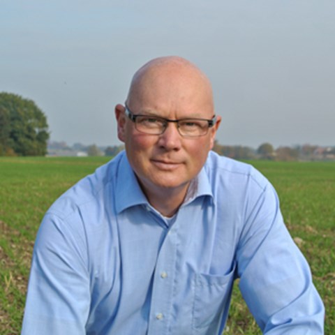 Porträttfoto av en man i blå skjorta på ett fält. Foto.