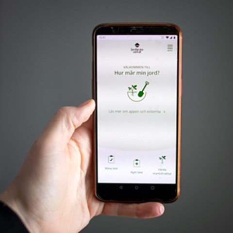 En hand håller i en mobiltelefon som visar appen "Hur mår din jord". Foto.
