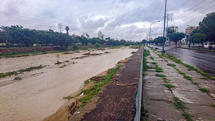 A brown river next to asphalt and a city. Photo. 