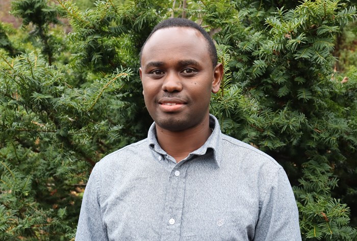 PhD student Marius Tuyishime against a pine tree background 