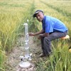 A man kneeling in a field, inspecting a water meter.