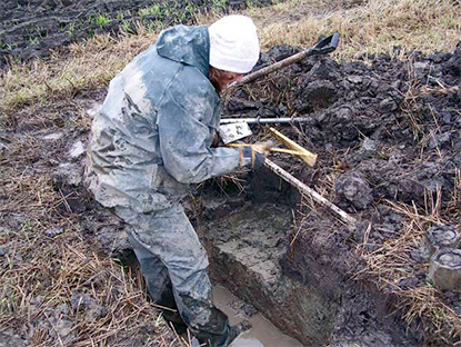 Woman in muddy field measures something, photo.