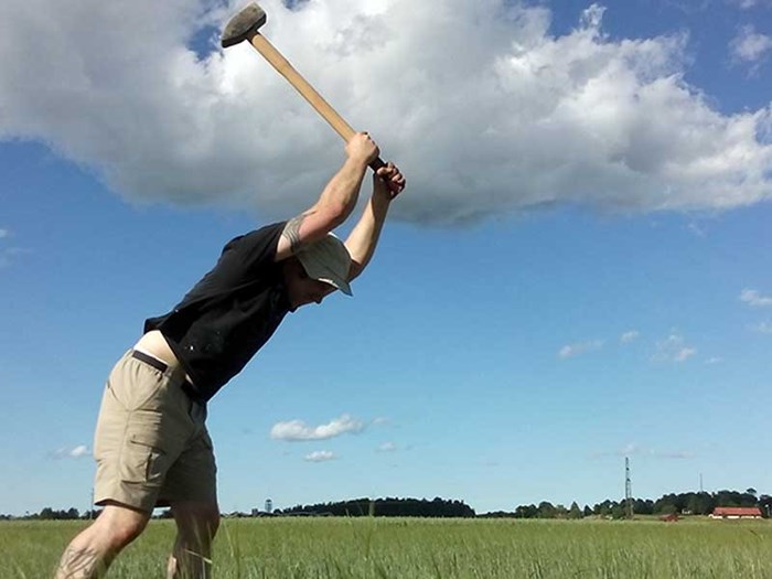 A man swings a hoe against a blue sky, photo.