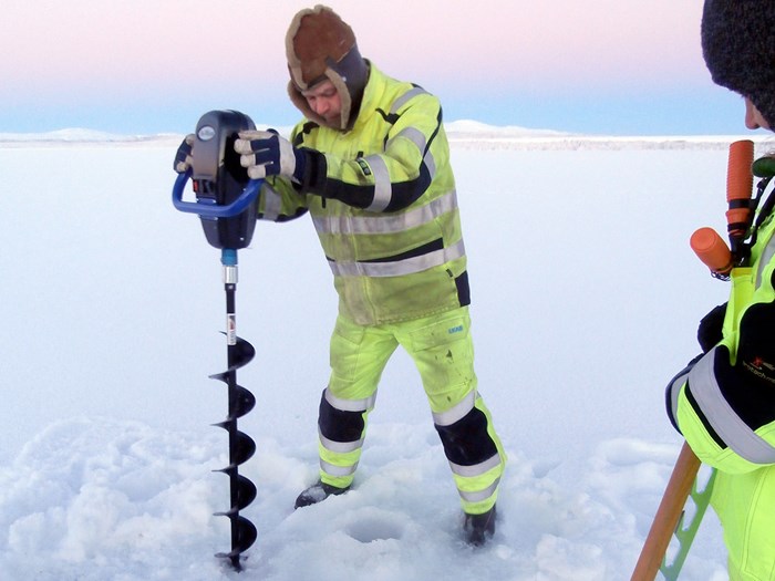 Two people in yellow overalls drill holes in the ice, photo.