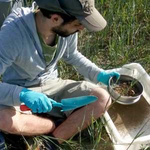 A man in a cap is sitting on the ground with soil in his hand, photo.