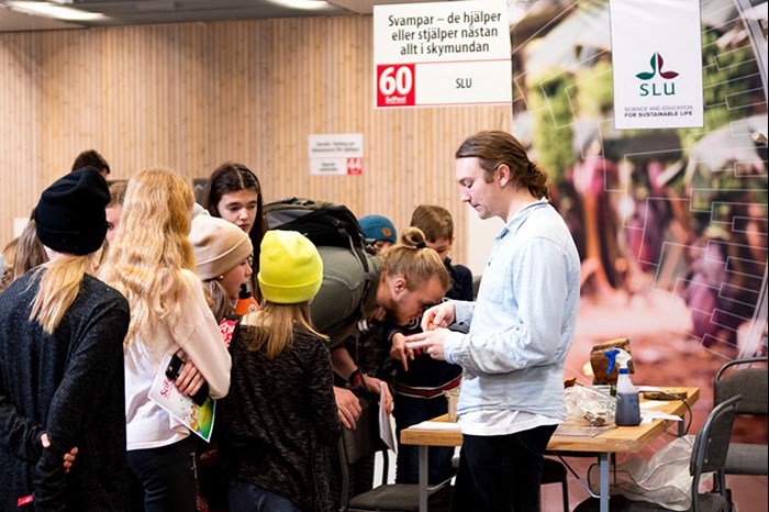 Studenter står framför en forskare och lyssnar, foto.
