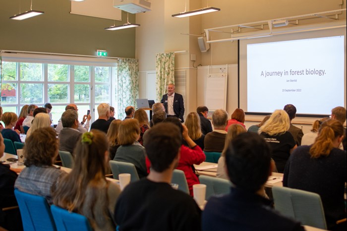A person is speaking in front of a large group in a lecture hall. Photo.